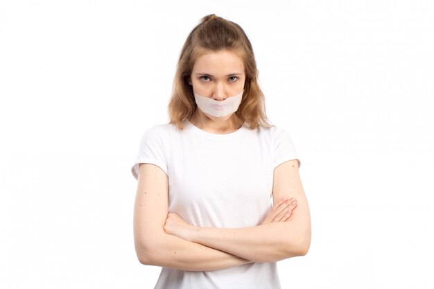 Una vista frontal joven mujer en camiseta blanca con vendaje blanco alrededor de su boca disgustó miedo en el blanco