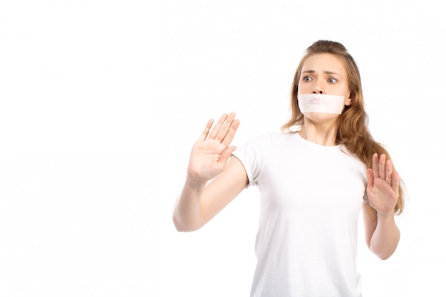 Una vista frontal joven mujer en camiseta blanca con vendaje blanco alrededor de su boca miedo cuidadoso en el blanco