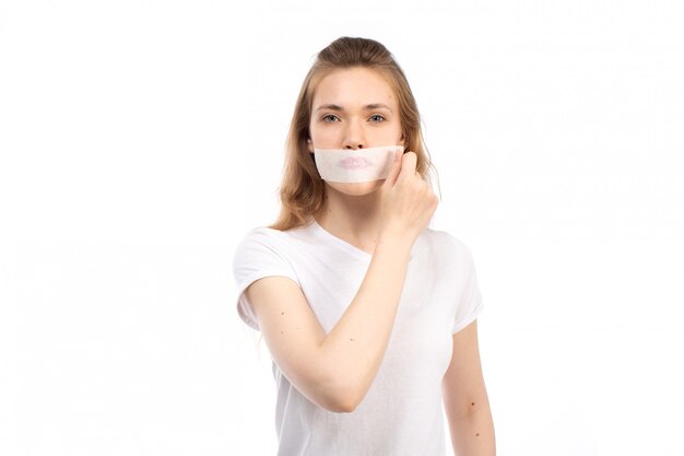 Una vista frontal joven mujer en camiseta blanca con vendaje blanco alrededor de su boca quitándose en el blanco