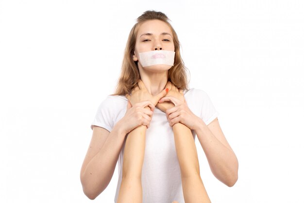 Una vista frontal joven mujer en camiseta blanca con vendaje blanco alrededor de su boca recibiendo amenazas físicas en el blanco