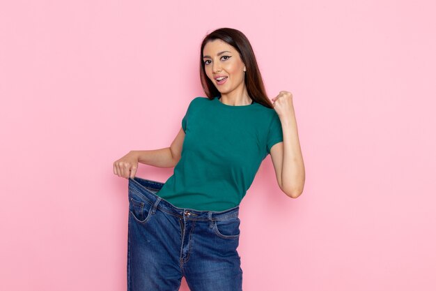 Vista frontal joven mujer en camiseta verde comprobando su cintura en la pared rosa claro cintura deporte ejercicio entrenamientos belleza delgada atleta femenina