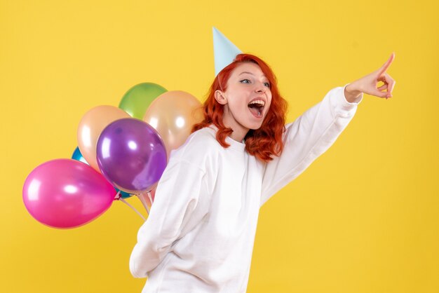 Vista frontal joven mujer escondiendo lindos globos de colores en amarillo