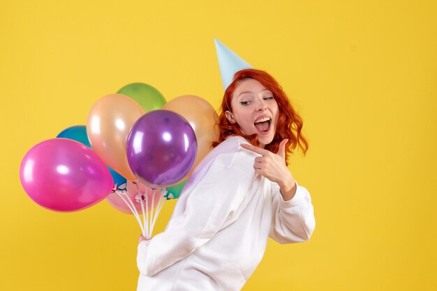 Vista frontal joven mujer escondiendo lindos globos de colores en amarillo