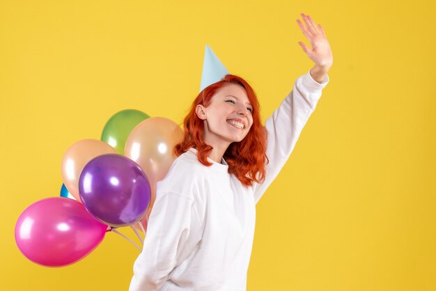 Vista frontal joven mujer escondiendo lindos globos de colores en el escritorio amarillo año nuevo color emoción regalo niño mujer