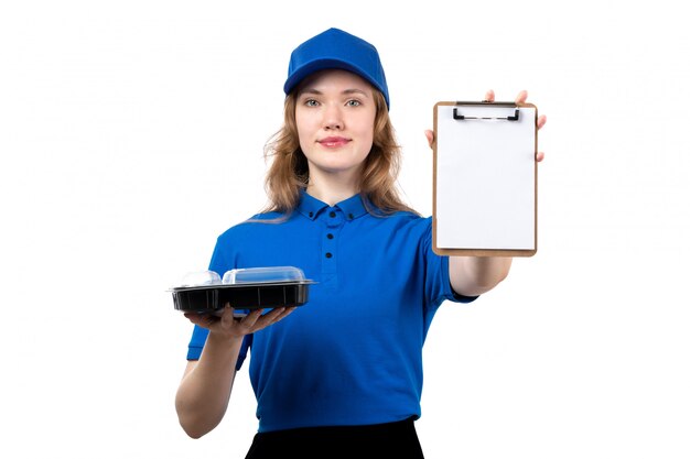 Una vista frontal joven mujer mensajero en camisa azul gorra azul y pantalón negro sosteniendo tazón con comida y bloc de notas en blanco