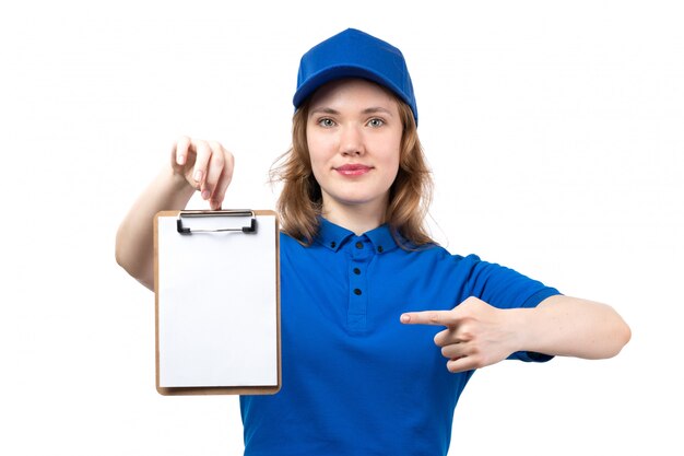 Una vista frontal joven mujer mensajero en camisa azul gorra azul sonriendo sosteniendo el bloc de notas de firma en blanco