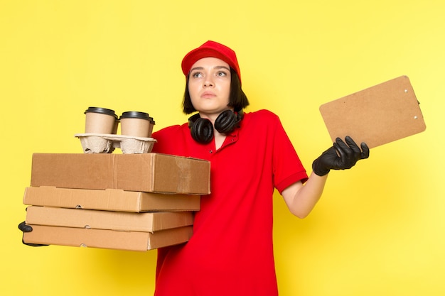 Una vista frontal joven mujer mensajero en rojo uniforme guantes negros y gorra roja con cajas de comida y tazas de café
