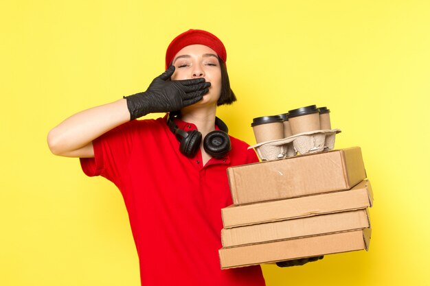 Foto gratuita una vista frontal joven mujer mensajero en rojo uniforme guantes negros y gorra roja con paquetes de alimentos y cajas