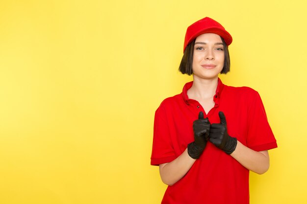 Una vista frontal joven mujer mensajero en rojo uniforme guantes negros y gorra roja posando con sonrisa
