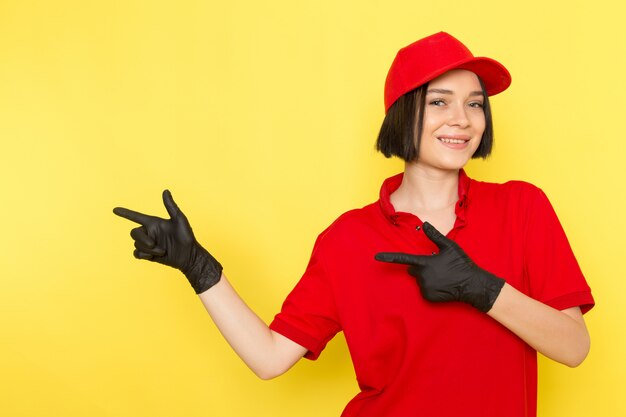 Una vista frontal joven mujer mensajero en rojo uniforme guantes negros y gorra roja posando con sonrisa