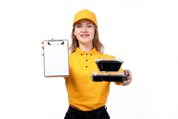 Foto gratuita una vista frontal joven mujer mensajero trabajadora del servicio de entrega de alimentos sonriendo sosteniendo el bloc de notas y cuencos con comida en blanco