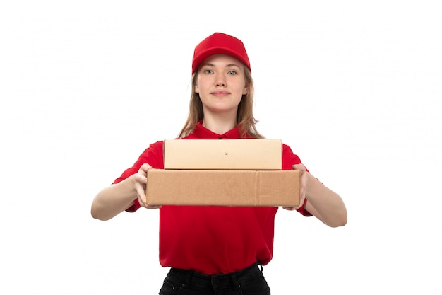 Una vista frontal joven mujer mensajero trabajadora del servicio de entrega de alimentos sonriendo sosteniendo cajas con comida en blanco