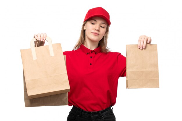 Una vista frontal joven mujer mensajero trabajadora del servicio de entrega de alimentos sonriendo sosteniendo paquetes de entrega de alimentos en blanco