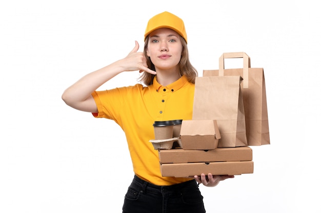 Una vista frontal joven mujer mensajero trabajadora del servicio de entrega de alimentos sosteniendo tazas de café paquetes de alimentos mostrando señal de llamada telefónica en blanco