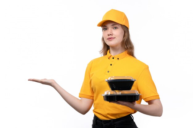 Una vista frontal joven mujer mensajero trabajadora del servicio de entrega de alimentos con tazones de comida y sonriendo en blanco