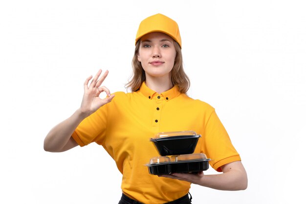 Una vista frontal joven mujer mensajero trabajadora del servicio de entrega de alimentos con tazones de comida y sonriendo en blanco