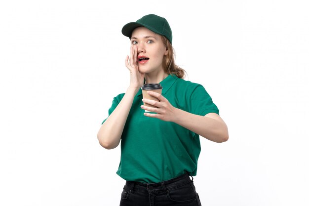 Una vista frontal joven mujer mensajero en uniforme verde con taza de café con expresión divertida en blanco