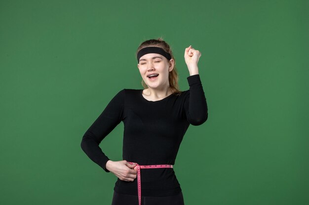 Vista frontal joven mujer midiendo su cintura con centímetro sobre fondo verde atleta negro mujer color salud entrenamiento ajuste cuerpo deportivo