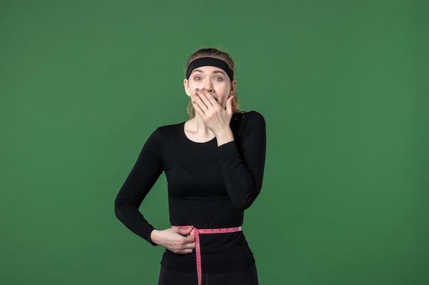 Vista frontal joven mujer midiendo su cuerpo con centímetro sobre fondo verde atleta mujer color salud cuerpo deportivo en forma negra