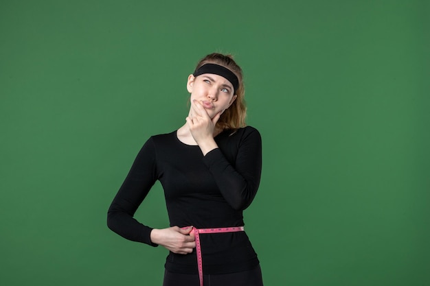 Vista frontal joven mujer midiendo su cuerpo con centímetro sobre fondo verde atleta mujer color salud cuerpo entrenamiento ajuste deporte
