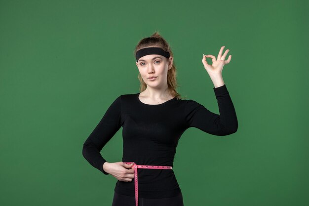 Vista frontal joven mujer midiendo su cuerpo con centímetro sobre fondo verde atleta mujer color salud cuerpo negro ajuste deporte