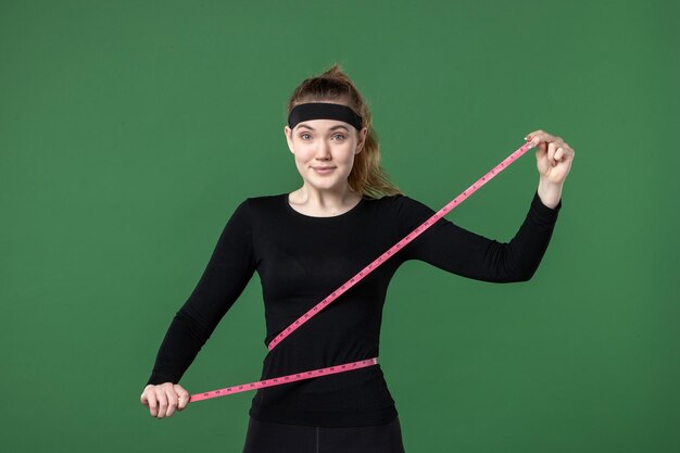 Vista frontal joven mujer midiendo su cuerpo con centímetro sobre fondo verde deporte color salud cuerpo mujer atleta ajuste negro