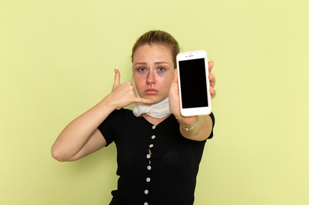 Vista frontal joven mujer sintiéndose muy enferma y enferma sosteniendo su teléfono en la pared verde claro enfermedad medicina enfermedad