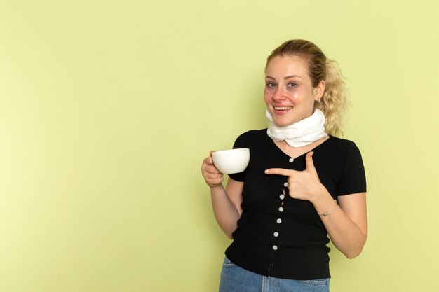 Vista frontal joven mujer sintiéndose muy enferma y enferma sosteniendo una taza de café sonriendo en la pared verde enfermedad medicina enfermedad salud