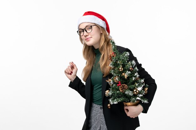 Vista frontal joven mujer sosteniendo árbol de vacaciones en escritorio blanco juguete año nuevo navidad