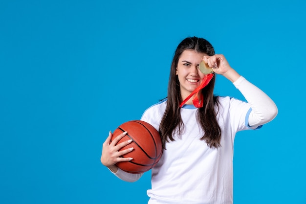 Vista frontal joven mujer sosteniendo baloncesto en pared azul