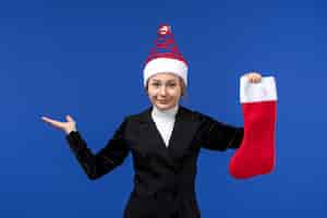 Foto gratuita vista frontal joven mujer sosteniendo calcetín rojo de navidad en la pared azul vacaciones de año nuevo humano