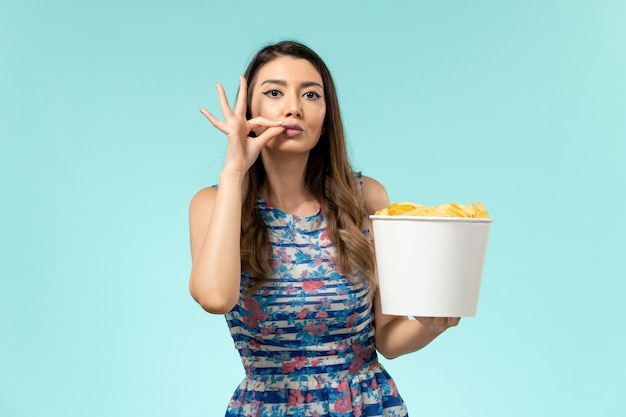 Foto gratuita vista frontal joven mujer sosteniendo la canasta con patatas fritas en la superficie azul claro