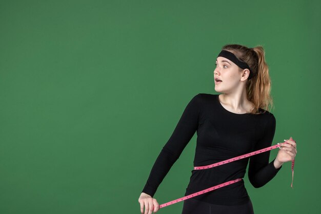 Vista frontal joven mujer sosteniendo centímetro para medir el cuerpo sobre fondo verde atleta negro mujer color ajuste deporte entrenamiento corporal