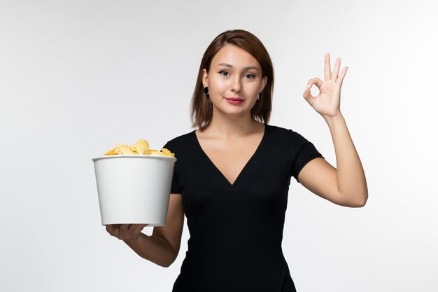 Vista frontal joven mujer sosteniendo la cesta con papas fritas y sonriendo sobre superficie blanca