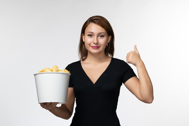 Vista frontal joven mujer sosteniendo la cesta con papas fritas y sonriendo sobre superficie blanca