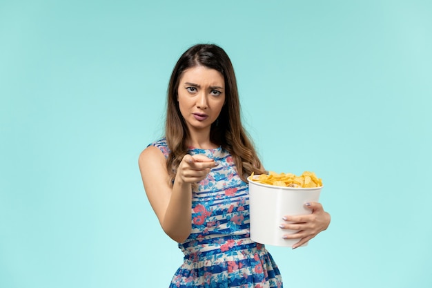 Vista frontal joven mujer sosteniendo la cesta con patatas fritas en la superficie azul