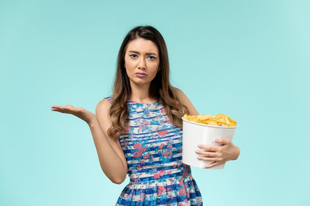 Vista frontal joven mujer sosteniendo la cesta con patatas fritas en la superficie azul