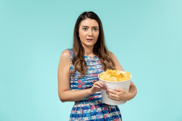 Vista frontal joven mujer sosteniendo la cesta con patatas fritas viendo la película en la superficie azul