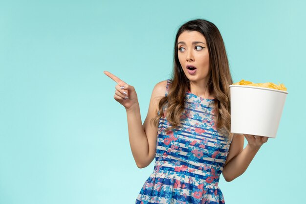 Vista frontal joven mujer sosteniendo la cesta con patatas fritas viendo la película en la superficie azul