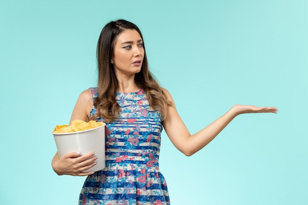 Vista frontal joven mujer sosteniendo la cesta con patatas fritas viendo la película en la superficie azul