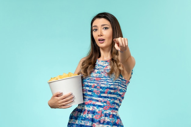 Vista frontal joven mujer sosteniendo la cesta con patatas fritas viendo la película en la superficie azul