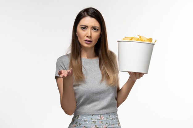 Vista frontal joven mujer sosteniendo chips mientras ve la película en el escritorio blanco