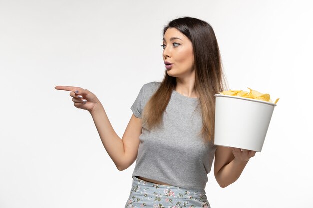 Vista frontal joven mujer sosteniendo chips mientras ve la película en el escritorio blanco
