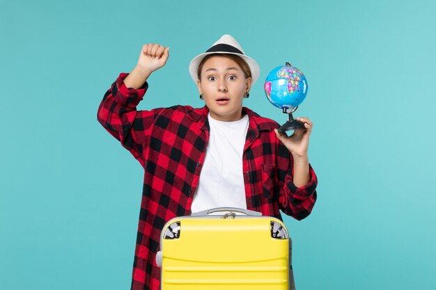 Vista frontal joven mujer sosteniendo globo terráqueo y preparándose para viaje en el espacio azul