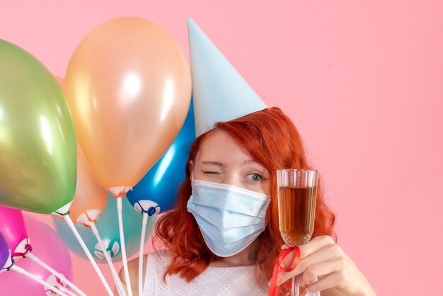 Vista frontal joven mujer sosteniendo globos de colores y copa de champán en una rosa