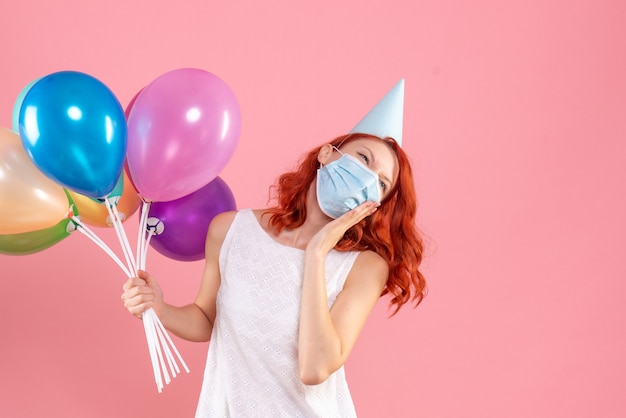 Vista frontal joven mujer sosteniendo globos de colores en máscara estéril en rosa