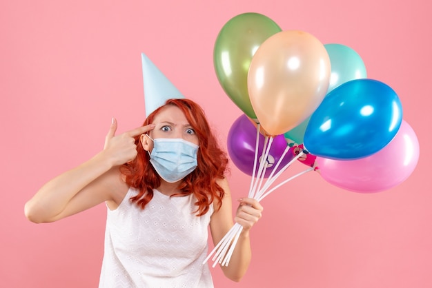 Foto gratuita vista frontal joven mujer sosteniendo globos de colores en máscara estéril en rosa