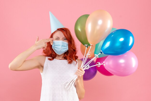 Vista frontal joven mujer sosteniendo globos de colores en máscara estéril en rosa