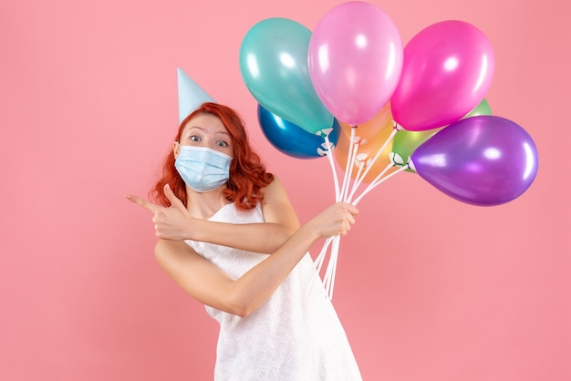 Vista frontal joven mujer sosteniendo globos de colores en máscara en rosa claro