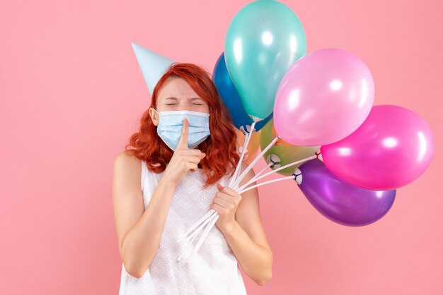 Vista frontal joven mujer sosteniendo globos de colores en máscara en rosa claro